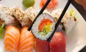 Chopsticks trzymają rolkę sushi z łososiem i ogórkiem. Obok nigiri z łososiem i tuńczykiem. To inspiracja, jak zrobić sushi!