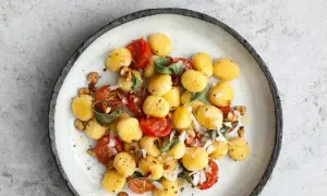 Pyszne makaron gnocchi z pomidorkami, orzechami i szałwią na talerzu.