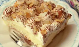 Pyszne ciasto na krakersach z kremem i bitą śmietaną, posypane kakao i płatkami migdałów. Idealne na deser!
