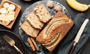 Szybkie fit ciasto bananowe z kawałkami czekolady i bananem na wierzchu, obok plasterki banana, orzechy i cynamon.