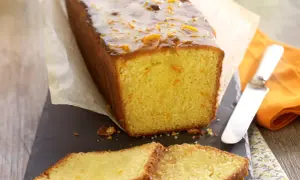 Wilgotne ciasto pomarańczowe z błyszczącą glazurą i kandyzowanymi skórkami pomarańczy, pokrojone na kromki.