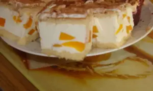 Sernik z bitą śmietaną Siostry Anastazji, z kawałkami brzoskwiń, posypany kakao. Pyszny deser na talerzu.