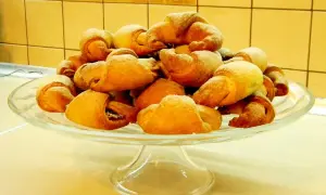 Rogaliki drożdżowe z przepisu babci, posypane cukrem pudrem, piętrzą się na szklanej paterze.