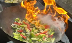 Ogień buchający z woka podczas przygotowywania aromatycznego stir fry z warzywami.