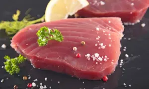 Surowy stek z tuńczyka, doprawiony solą i pieprzem, z plasterkiem cytryny i natką pietruszki. Gotowy do grillowania.