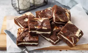 Szybkie ciasto z serem z wiaderka, czekoladowe brownie z kremową warstwą sera, ułożone na desce.