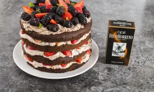 Obłędny tort czekoladowy z mascarpone i owocami: warstwy ciemnego ciasta przełożone kremem i świeżymi truskawkami, jeżynami i listkami mięty. Obok pudełko Cacao Decomorreno.
