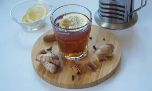Szklanka aromatycznej herbaty z cytryną, obok świeży imbir do herbaty, laski cynamonu i goździki. Idealne na chłodne dni.