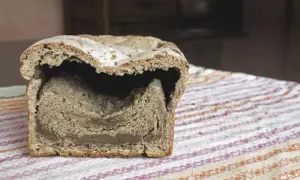 Chleb z zakalcem, z dziurą w środku, leży na kolorowym obrusie.