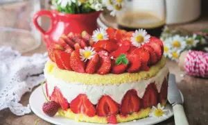 Puszysty biszkopt z truskawkami i mascarpone, ozdobiony świeżymi owocami i stokrotkami. Idealny na letnie popołudnie.
