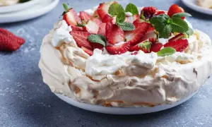Pyszny tort bezowy z mascarpone i bitą śmietaną, ozdobiony świeżymi truskawkami i miętą.