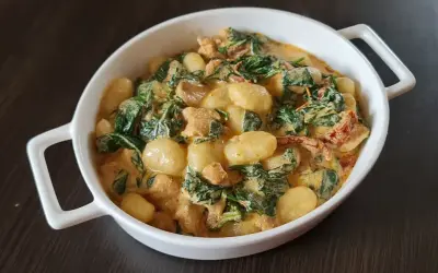Pyszne gnocchi z kurczakiem w sosie śmietanowym, ze szpinakiem i suszonymi pomidorami, podane w białej misie.