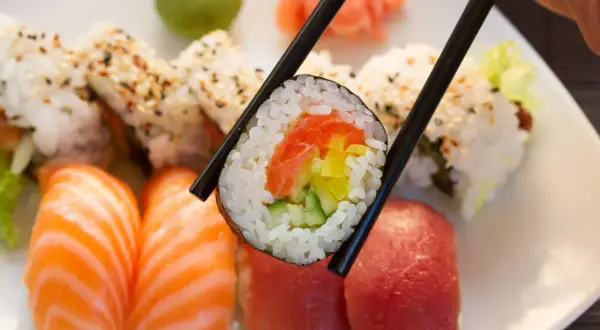 Chopsticks trzymają rolkę sushi z łososiem i ogórkiem. Obok nigiri z łososiem i tuńczykiem. To inspiracja, jak zrobić sushi!