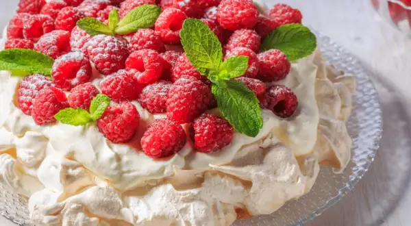 Beza Pavlova, która zawsze wychodzi, obficie udekorowana malinami i listkami mięty, posypana cukrem pudrem.