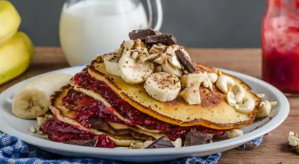 Stos puszystych, trzyskładnikowych placków bananowych z malinową konfiturą, bananami, orzechami i czekoladą.