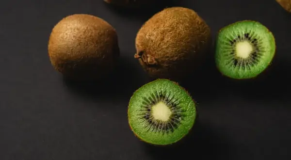 Kiwi właściwości: soczyste owoce, jeden przekrojony ukazuje zielony miąższ z czarnymi pestkami.