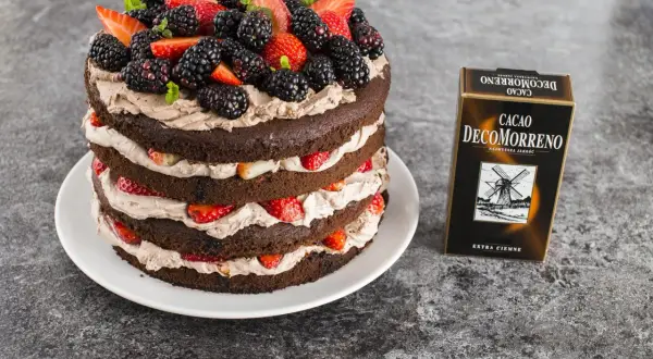 Obłędny tort czekoladowy z mascarpone i owocami: warstwy ciemnego ciasta przełożone kremem i świeżymi truskawkami, jeżynami i listkami mięty. Obok pudełko Cacao Decomorreno.