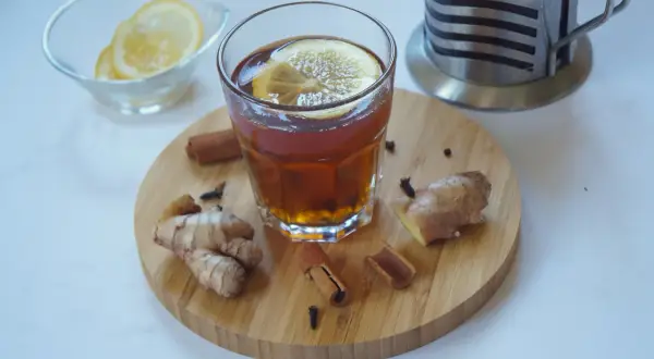 Szklanka aromatycznej herbaty z cytryną, obok świeży imbir do herbaty, laski cynamonu i goździki. Idealne na chłodne dni.