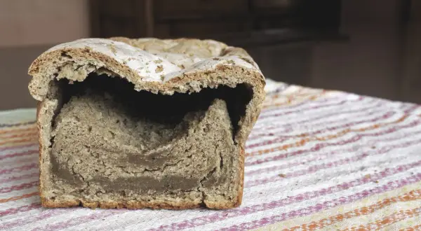 Chleb z zakalcem, z dziurą w środku, leży na kolorowym obrusie.