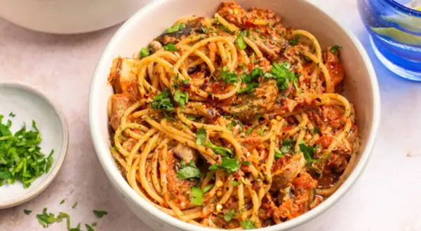 Miseczka spaghetti z sosem pomidorowym, grzybami i posiekaną natką pietruszki.