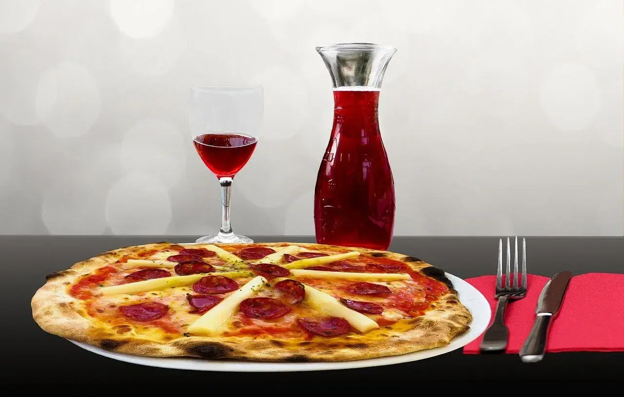 Pyszna pizza fritta z kiełbasą i szparagami, podana z kieliszkiem czerwonego wina i karafką. Idealna kolacja!