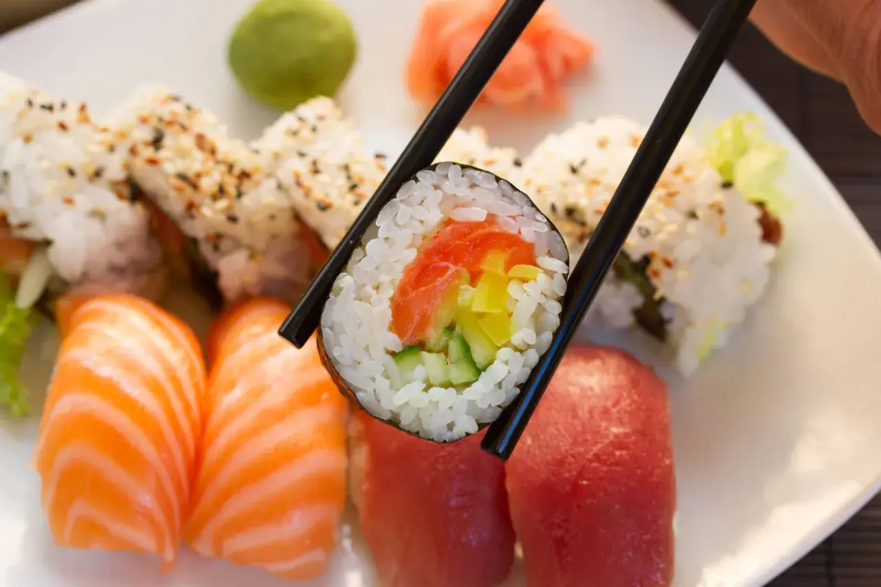 Chopsticks trzymają rolkę sushi z łososiem i ogórkiem. Obok nigiri z łososiem i tuńczykiem. To inspiracja, jak zrobić sushi!