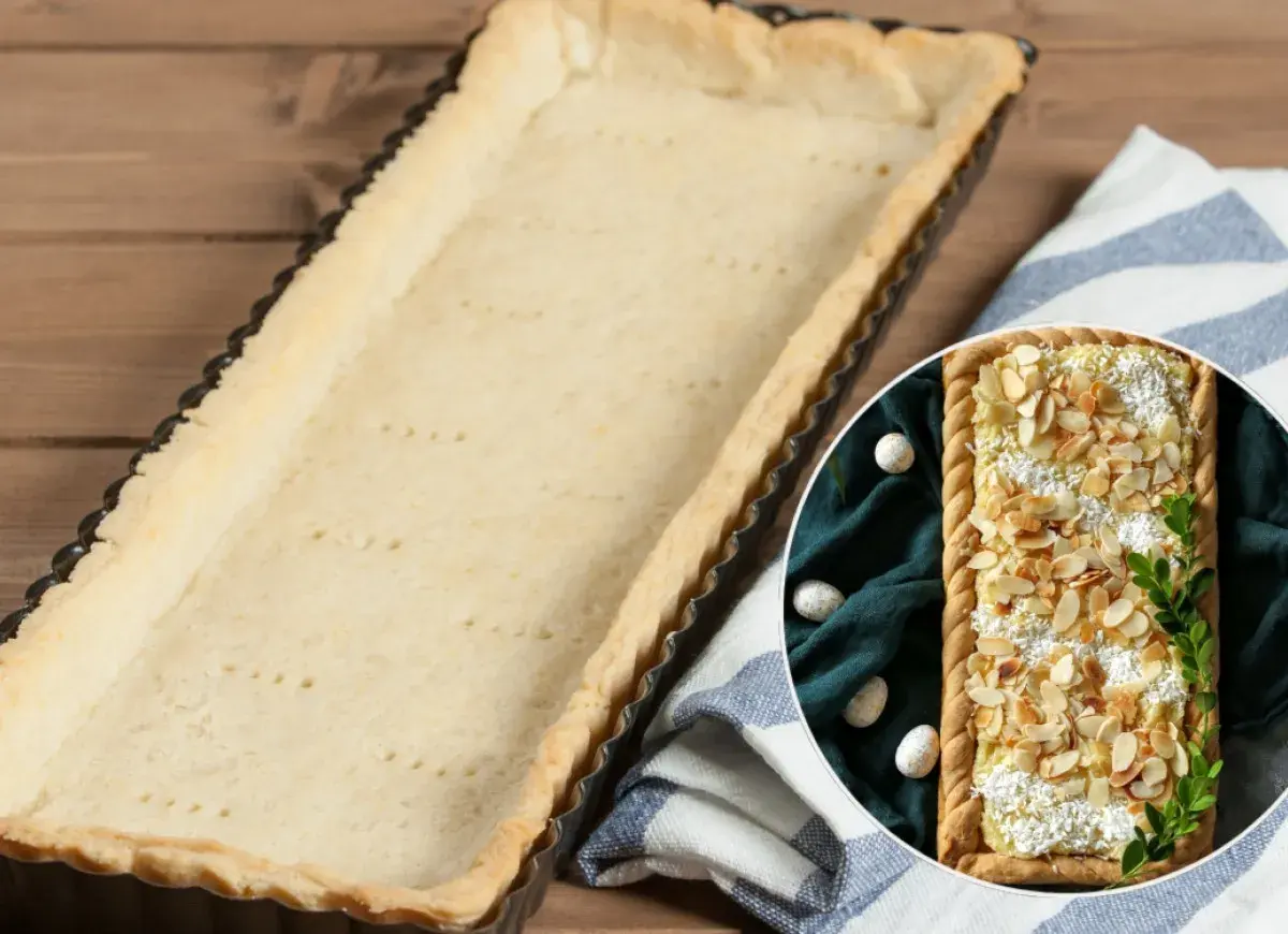 Pusta, upieczona masa do mazurka w formie czeka na nadzienie. Obok w okręgu widać gotowy mazurek z migdałami.