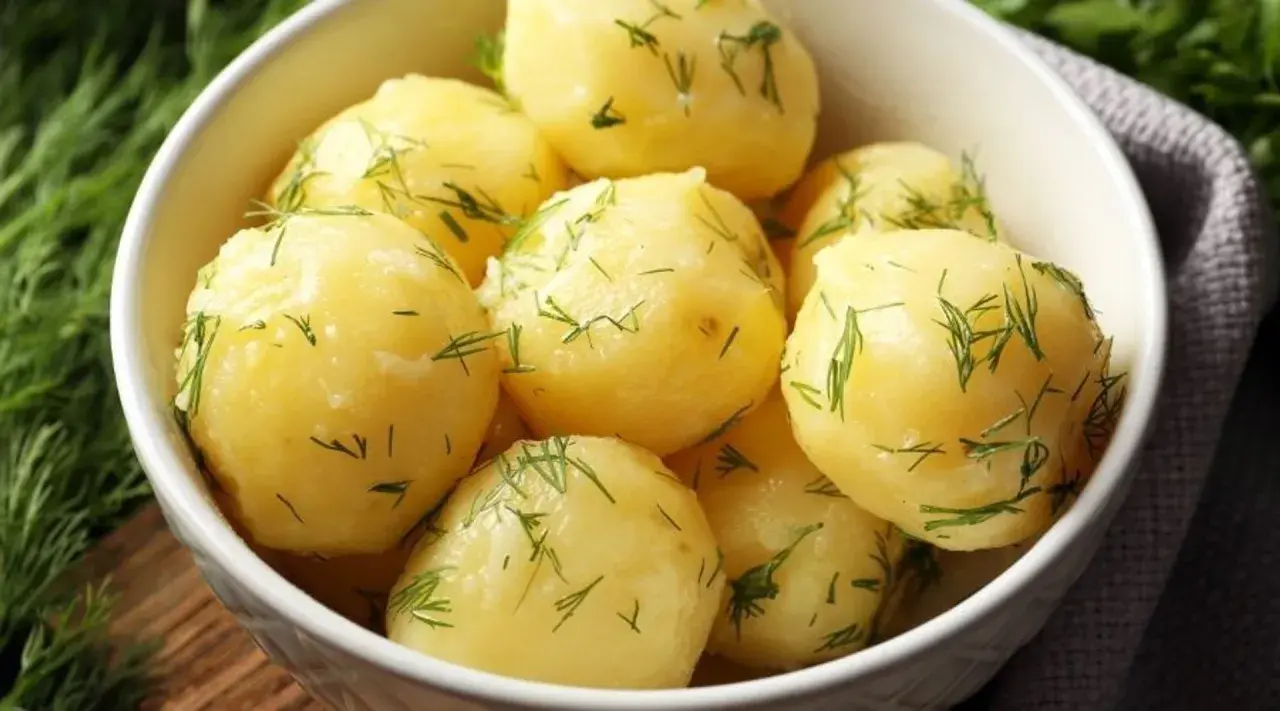 A white bowl filled with fluffy ziemniaki na parze, sprinkled with fresh dill.