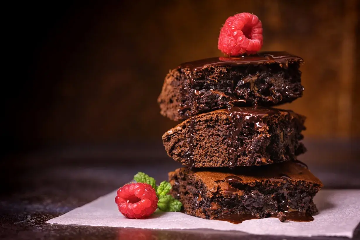 Stos pysznych, wilgotnych brownie z polewą czekoladową i malinami. Idealny brownie prosty przepis na domowe ciasto.