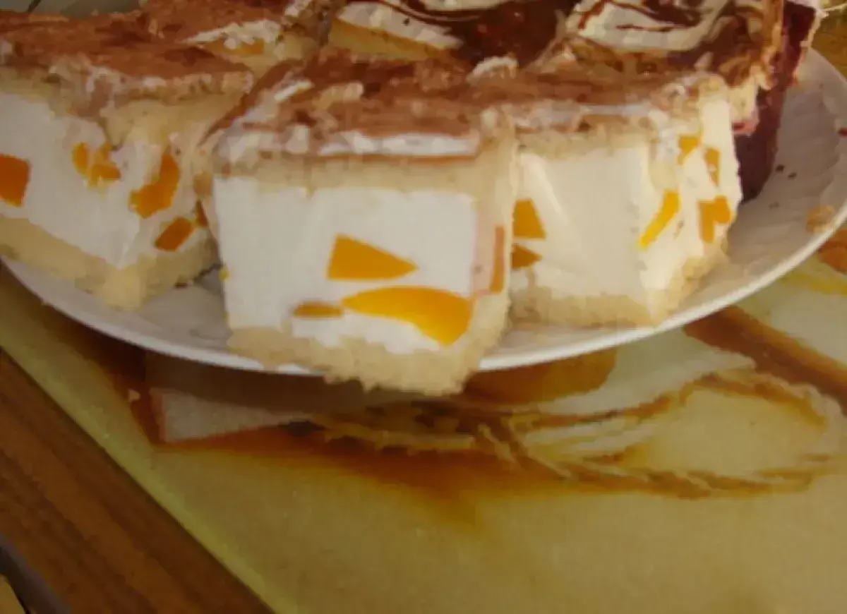 Sernik z bitą śmietaną Siostry Anastazji, z kawałkami brzoskwiń, posypany kakao. Pyszny deser na talerzu.