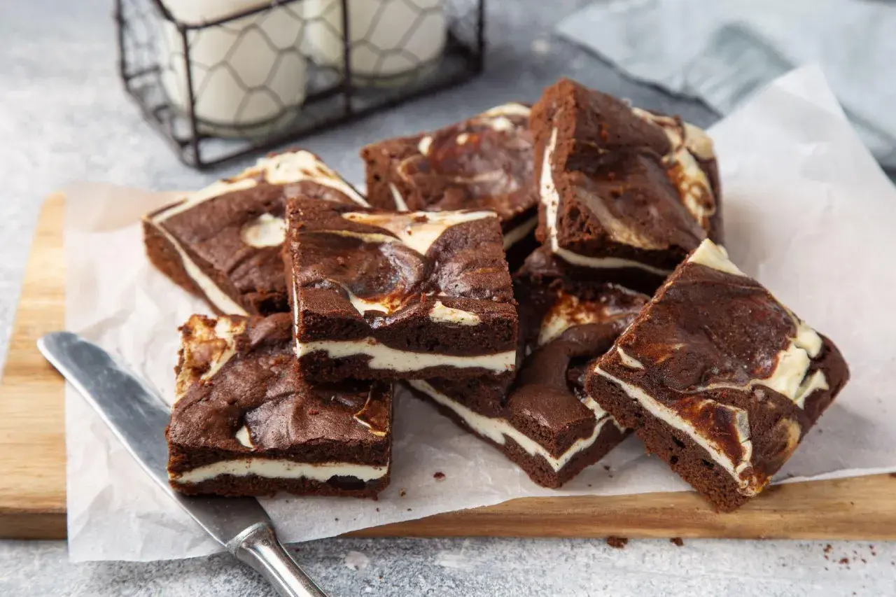 Szybkie ciasto z serem z wiaderka, czekoladowe brownie z kremową warstwą sera, ułożone na desce.