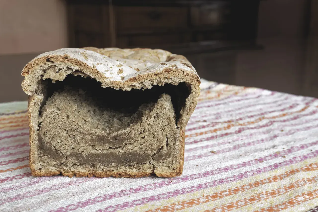 Chleb z zakalcem, z dziurą w środku, leży na kolorowym obrusie.