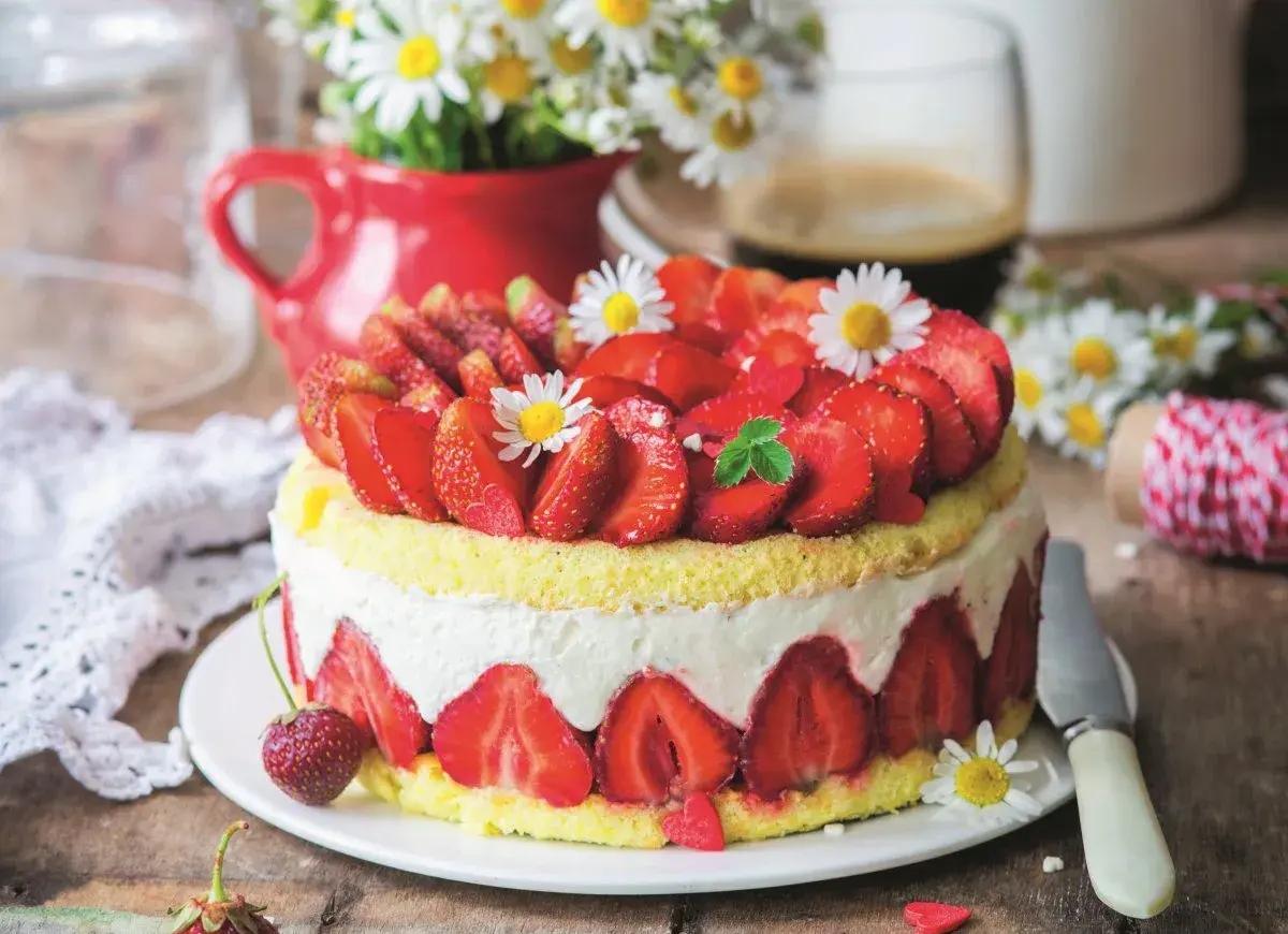 Puszysty biszkopt z truskawkami i mascarpone, ozdobiony świeżymi owocami i stokrotkami. Idealny na letnie popołudnie.