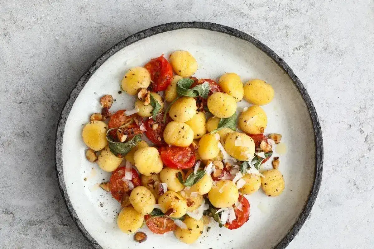 Pyszne makaron gnocchi z pomidorkami, orzechami i szałwią na talerzu.