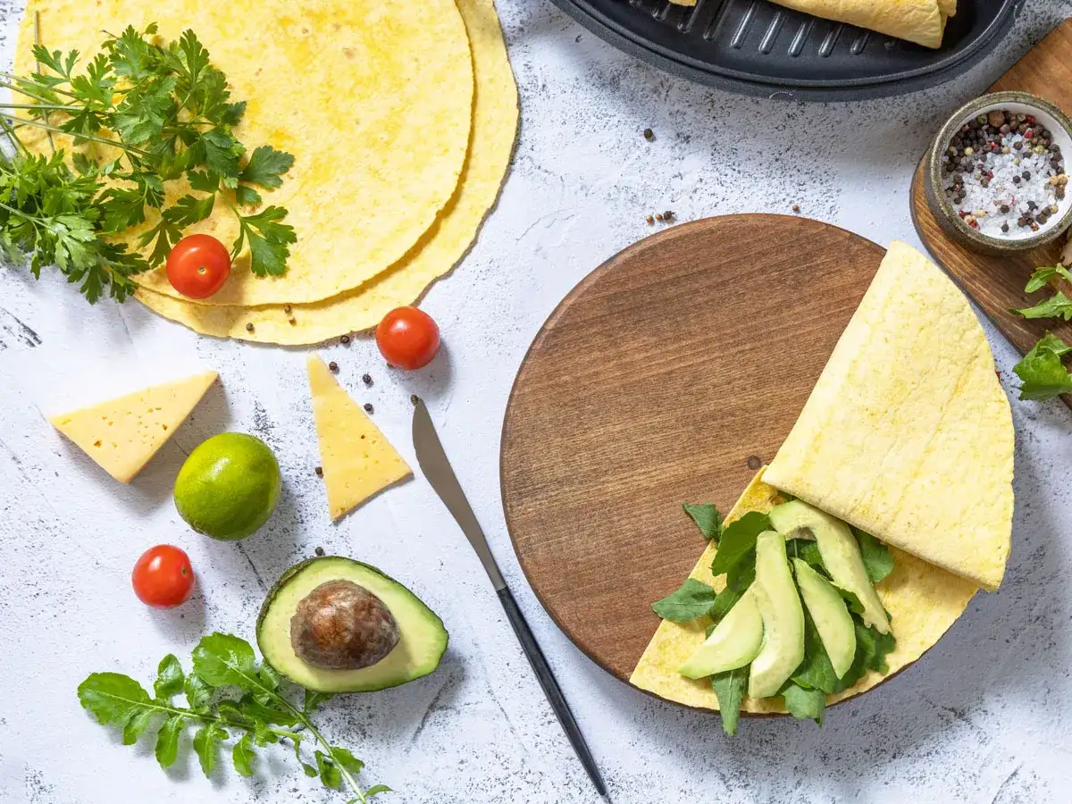 Składniki do keto tortilla przepis: awokado, pomidorki, ser, limonka, rukola i świeża natka.