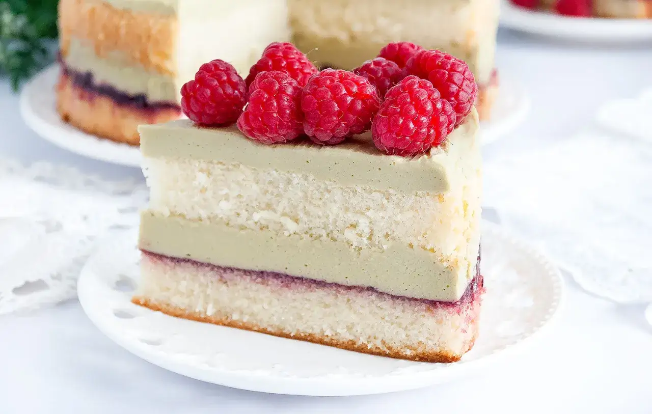 Pyszny tort pistacjowo malinowy, udekorowany świeżymi malinami, kusi warstwami biszkoptu i kremu.