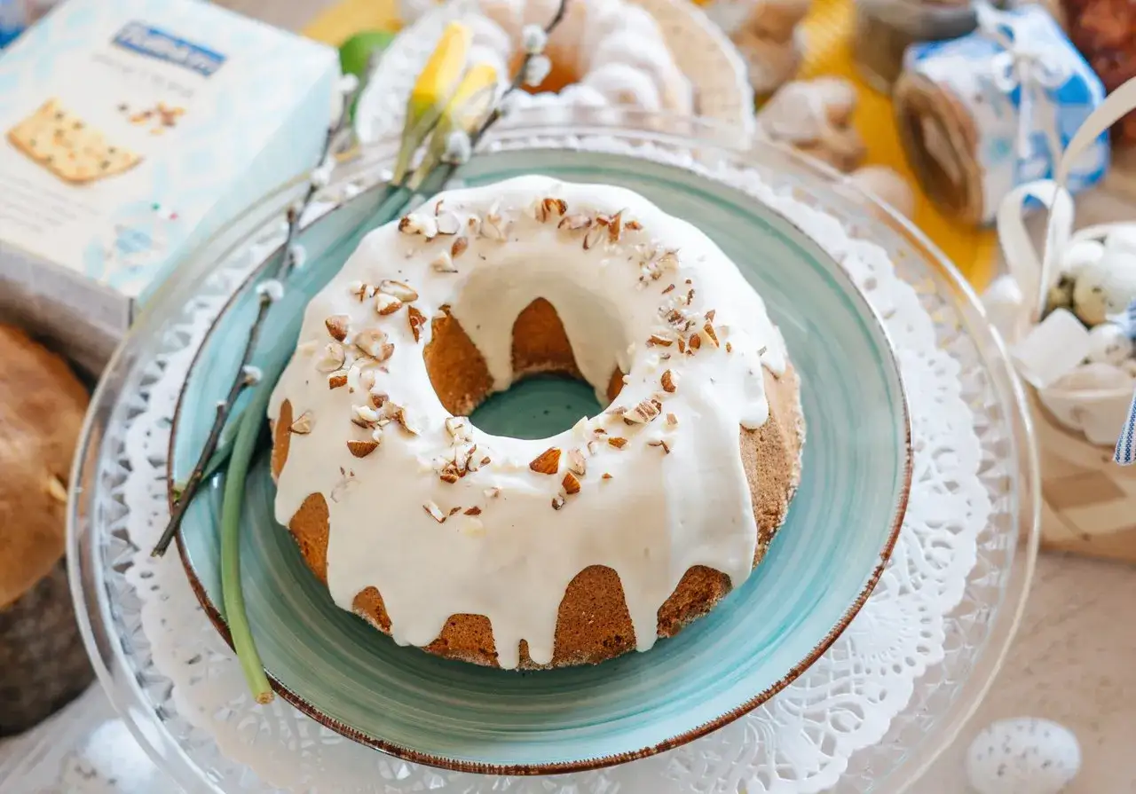 Babka piaskowa przepis babci, udekorowana lukrem i orzechami, na talerzu z wiosennymi ozdobami.