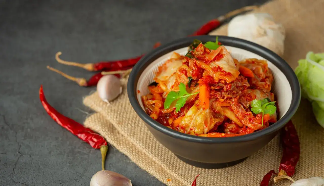 Miseczka z gotowym kimchi, obok suszone papryczki chili i czosnek. Idealne składniki, by dowiedzieć się, jak zrobić kimchi.
