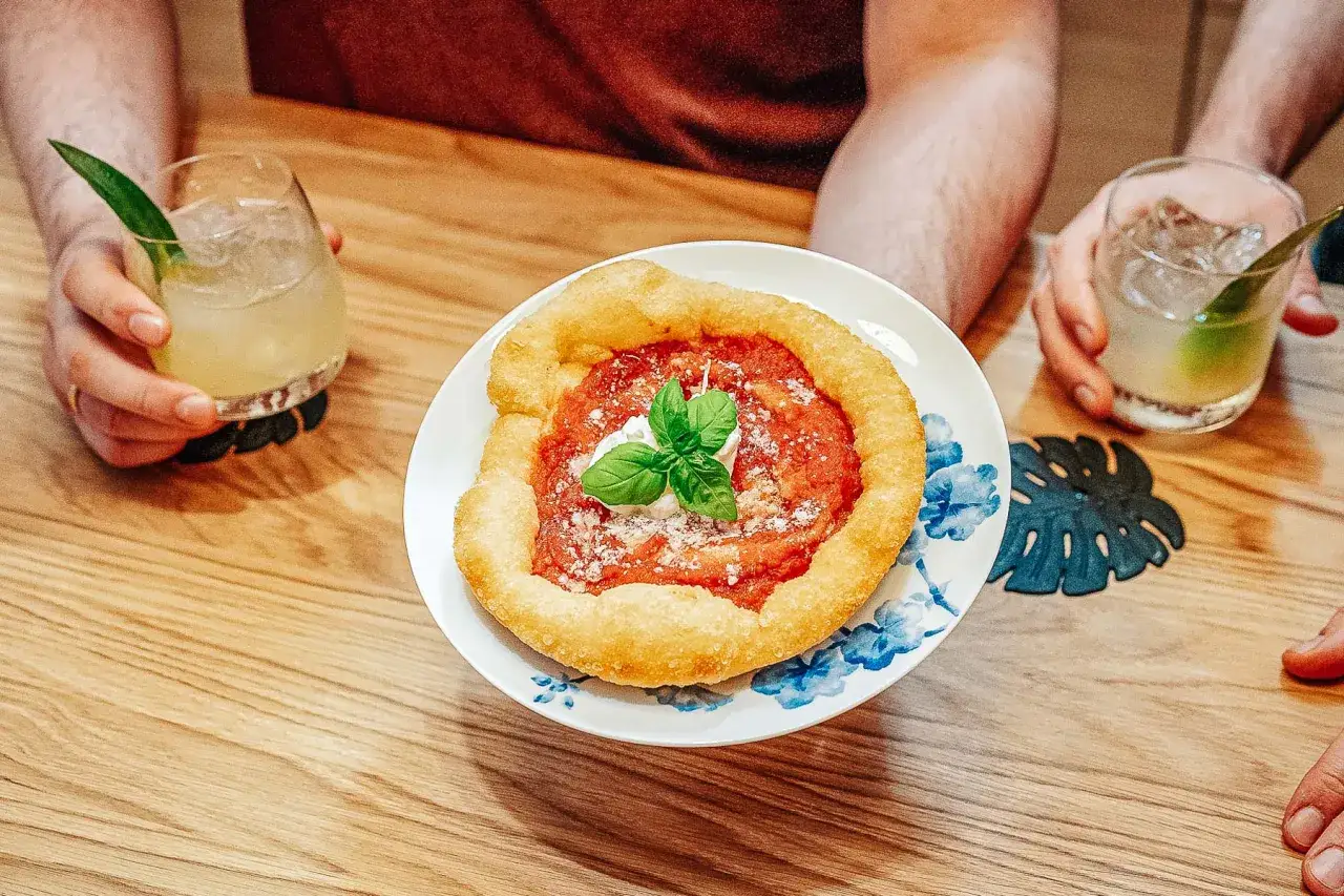 Pyszna pizza fritta z sosem pomidorowym, mozzarellą i bazylią na talerzu z niebieskimi kwiatami. Obok drinki z lodem.