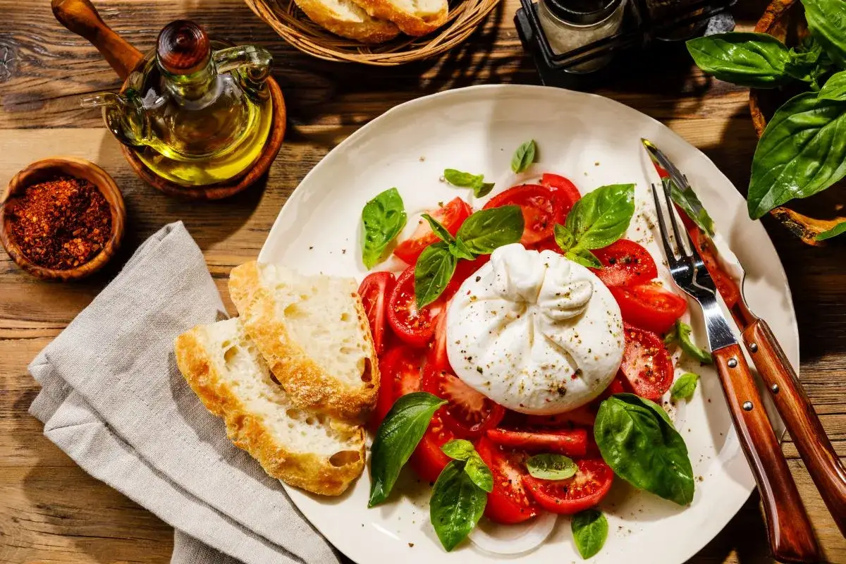 Ser burrata z pomidorami i bazylią, podany z chrupiącym pieczywem. Idealny sposób, by cieszyć się smakiem tego kremowego sera.
