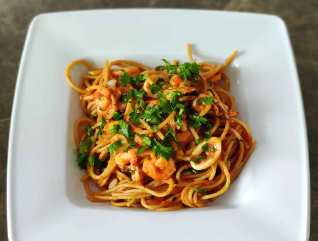 Pyszne linguini z owocami morza i pomidorowym sosem, posypane świeżą natką pietruszki.