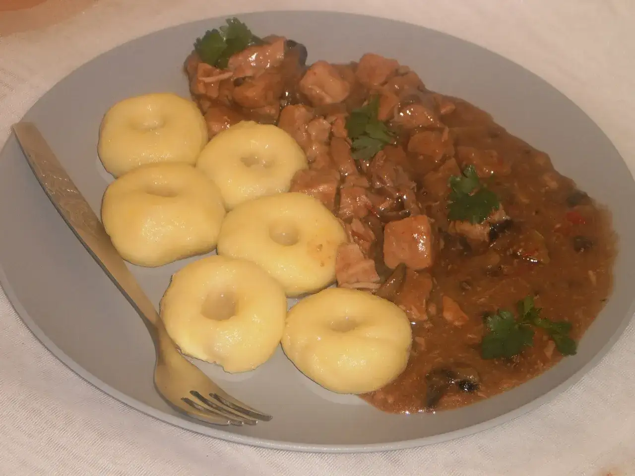 Pyszne kluski makaron gnocchi z gulaszem mięsnym i pieczarkami, ozdobione natką pietruszki.