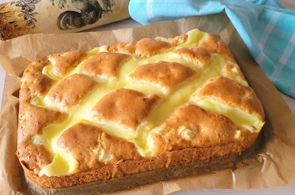 Wilgotne ciasto jogurtowe z budyniem, pieczone na papierze, z błękitnym ręcznikiem w kratkę w tle.