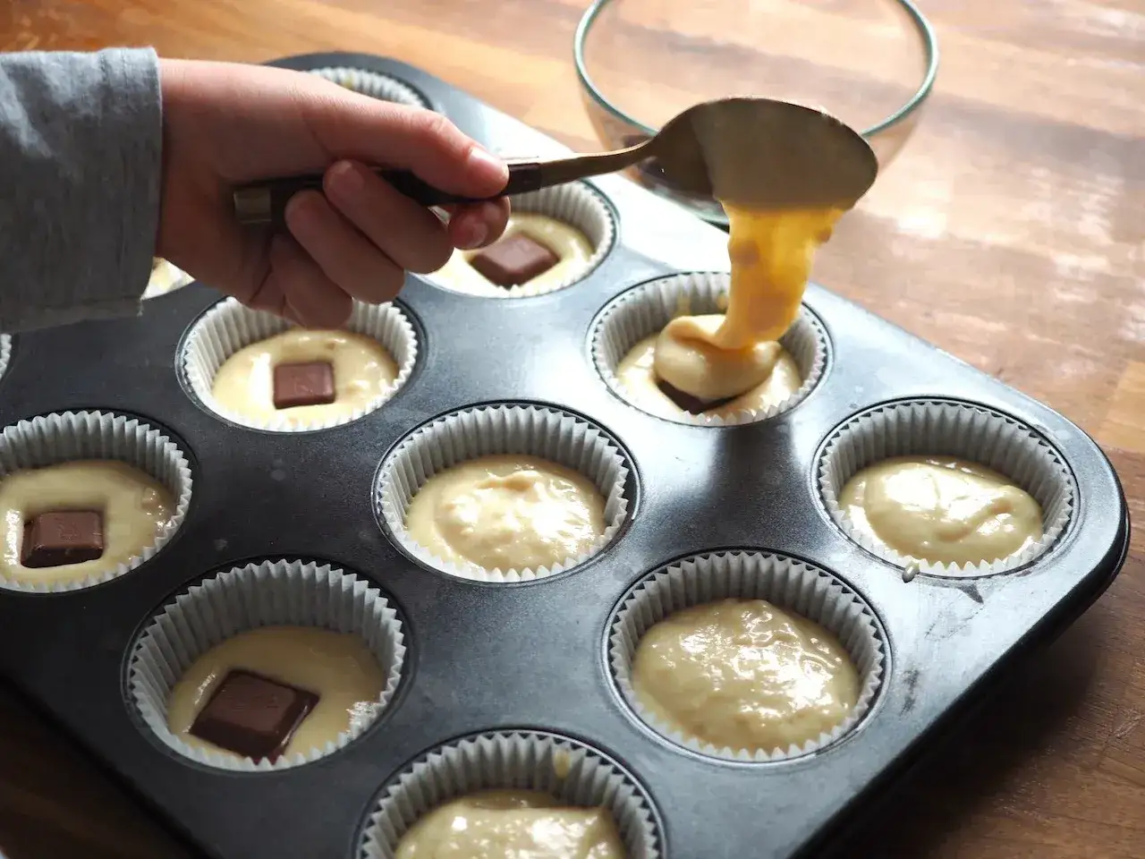 Dziecko przygotowuje pyszny przepis na muffinki, dodając kawałki czekolady do ciasta w foremkach.