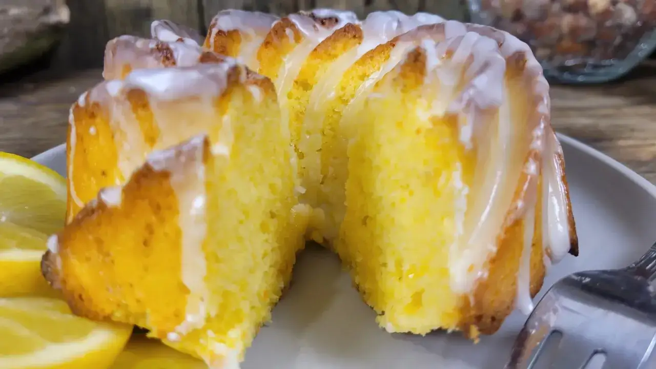 Babka cytrynowa bardzo wilgotna mniam, z lukrem i plasterkami cytryny na talerzu.