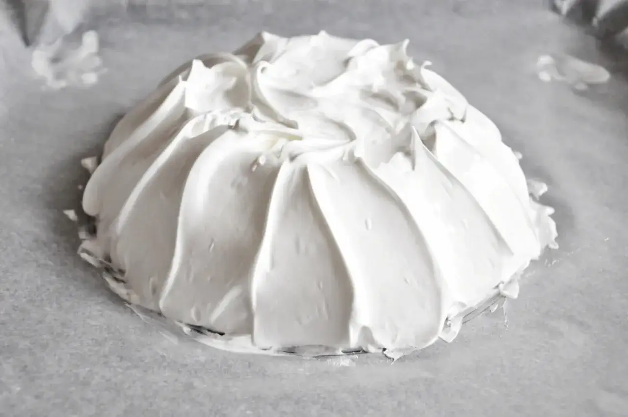 Beza pavlova która zawsze wychodzi, przygotowana na papierze do pieczenia. Jej puszysta, biała masa tworzy faliste wzory.