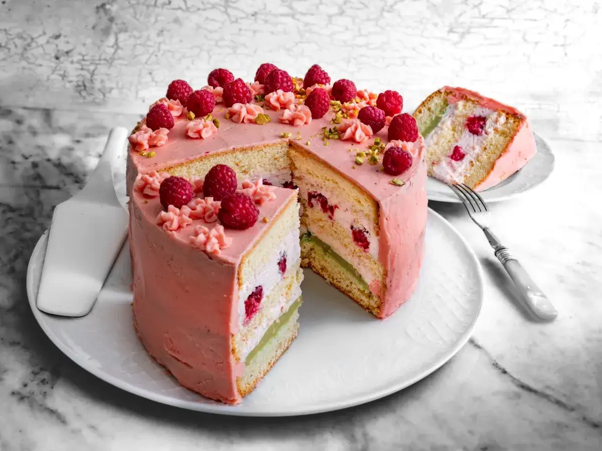 Pyszny tort z malinami i kremem malinowym z mascarpone, ozdobiony świeżymi malinami i pistacjami.