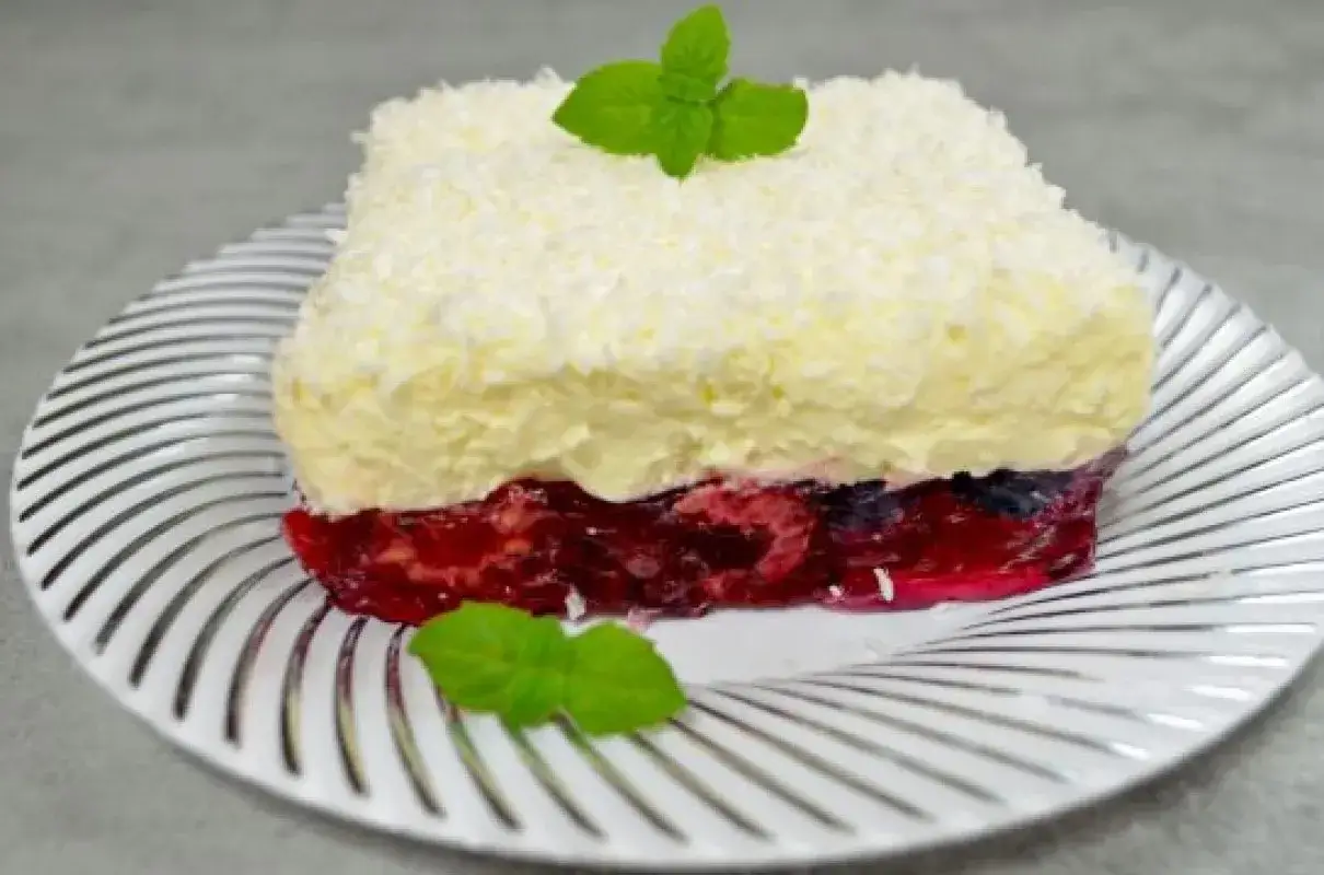Proste ciasto z serkiem mascarpone i galaretką owocową, posypane wiórkami kokosowymi i udekorowane miętą.