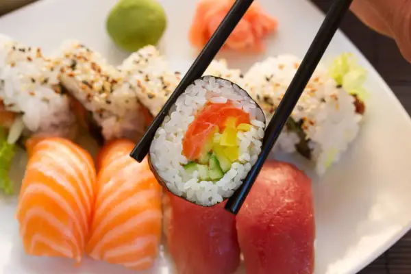 Chopsticks trzymają rolkę sushi z łososiem i ogórkiem. Obok nigiri z łososiem i tuńczykiem. To inspiracja, jak zrobić sushi!