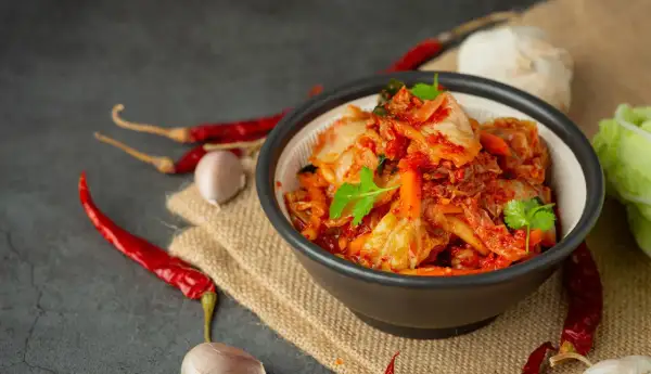 Miseczka z pikantnym kimchi, obok papryczki chili i czosnek. Idealne składniki, by dowiedzieć się, jak zrobić kimchi.